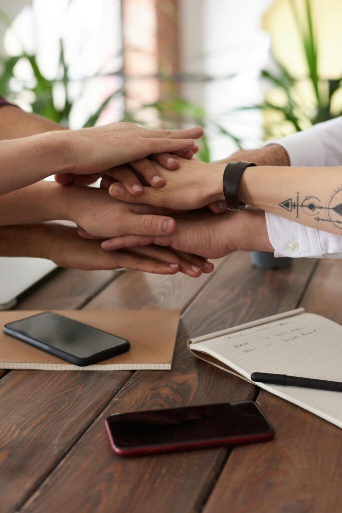 pexels-photo-3184431-3184431 Hands from a diverse team stack on a table symbolizing unity and teamwork in a modern office setting.