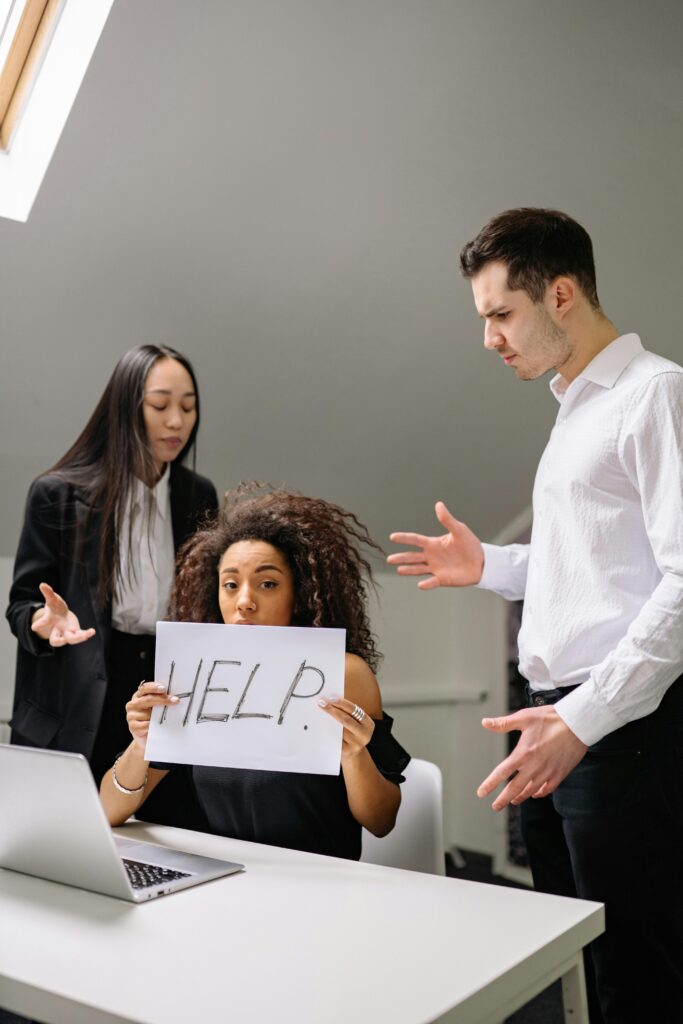 pexels-photo-7640786-7640786 Woman holding HELP sign surrounded by colleagues in a tense office situation.
